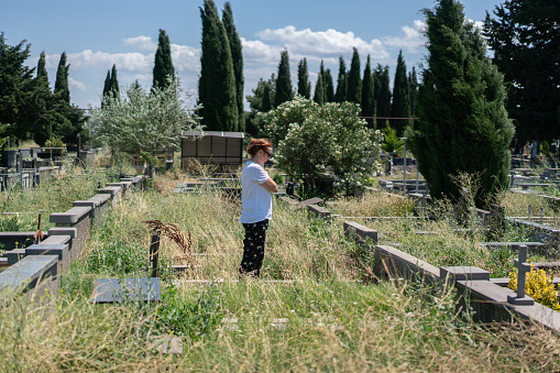The woman visits her father's grave in the cemetery and prays.