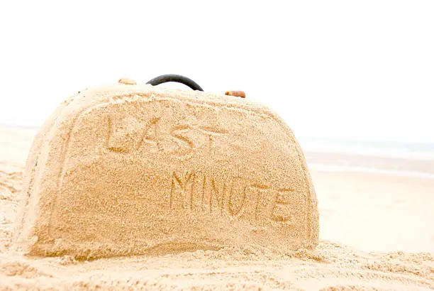 Last minute written on suitcase build out of sand on beach concept