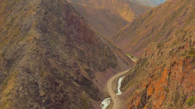 Drone scenic view of mountain river and road running along it with moving vehicles.
