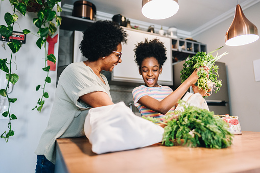 Mother and daughter talking and unpacking fruits and vegetables in the kitchen at apartment