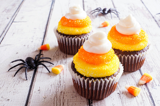 Halloween candy corn chocolate cupcakes over a rustic white wood table background