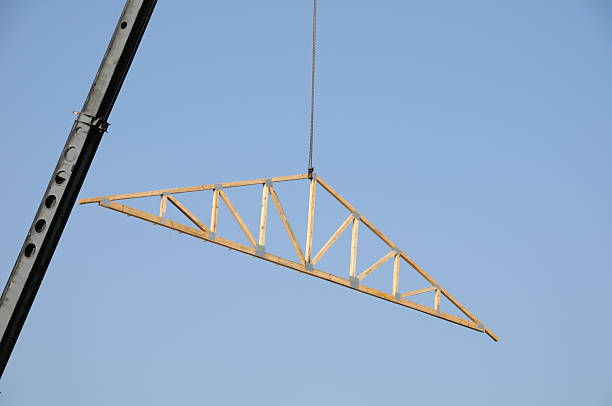 A wood roof truss being lifted by crane. The truus is held together by steel plates.