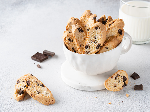 Coffee cup filled with black coffee on a white saucer with a chocolate chip cookie and spoon on a bright white background.