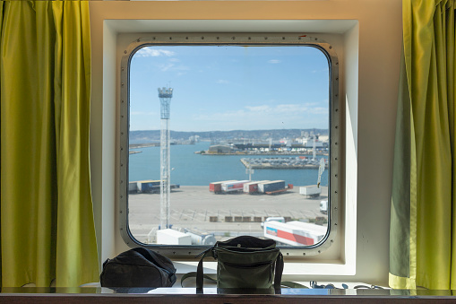 Porthole View on Marseille Docks from the ferry cabin. Part of the interior is shown with curtains and toiletries