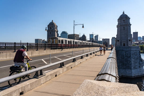 blick auf einen mann, der mit seinem fahrrad fährt, zug fährt und leute, die morgens auf dem longfellow bright spazieren gehen - boston skyline charles river blue stock-fotos und bilder