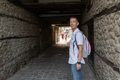 Smiling mid adult man during his walk around the old town. He is carrying a backpack and exploring the wonders of this interesting city.