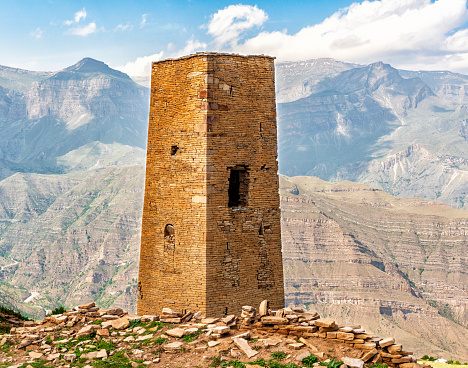 Russia, Dagestan, 05/19/2023, Goor village, watchtower of the 26th century. In front of the tower are processed stones from destroyed buildings. Mountain ranges, ravines, cliffs and abysses, steep slopes make up a wonderful extreme mountain landscape.