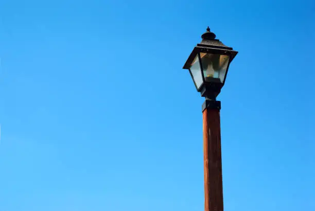 An old, vintage gaslight street lamp fixed on a tall red wooden pole isolated against a clear, deep blue summer sky. Copy space.