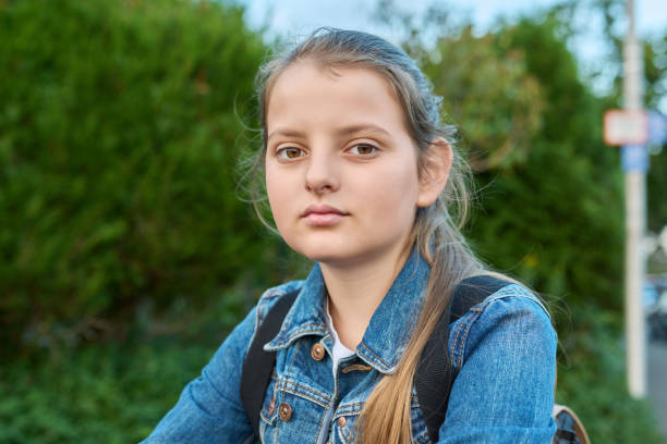 headshot portrait 10 years old girl with backpack outdoor, looking at camera - 10 11 years child human face female imagens e fotografias de stock