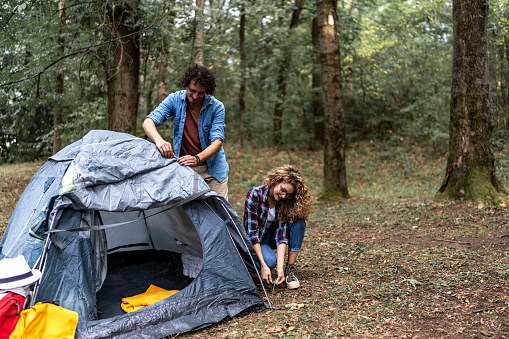 Young couple set up a tent together in forest. outdoor adventure, camping trip