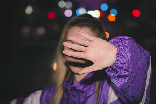 Woman in a sport jacket (90s style) poses against a blurry background of passing cars. City portrait hiding girl with bokeh illumination.