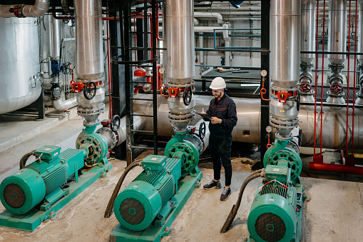 Young Caucasian engineer is taking notes, while examining the equipment in a heating plant.