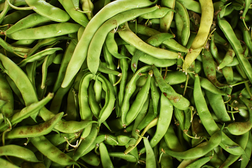 Fresh fava beans, peeled and in pods on a wooden table.