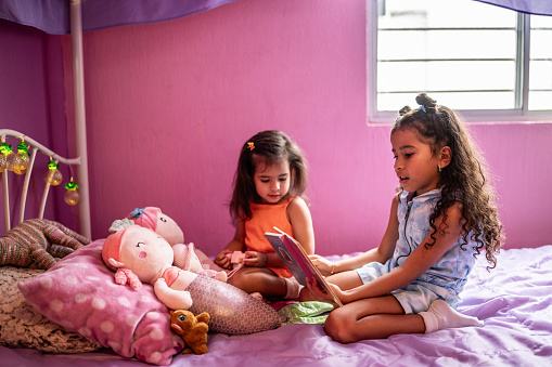 Girl child telling a story to her sister in the bedroom at home