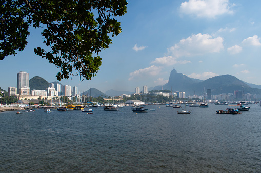 Rio de Janeiro, Brazil: Urca district, view of Guanabara Bay and the harbour for fishing boats with misty city ​​skyline and Christ the Redeemer on Corcovado Mountain on the background