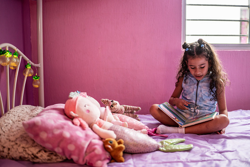 Girl child reading a book sitting on bed in the bedroom at home