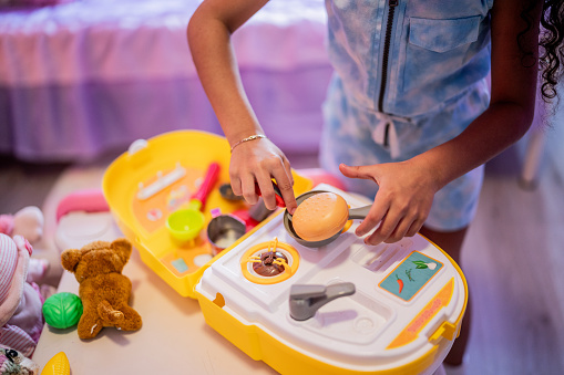Close-up of a girl child playing with cooking using toys in the bedroom at home