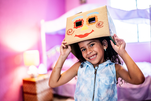 Portrait of a child girl with a painted cardboard box on head at home