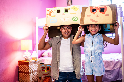 Portrait of father and daughter with a painted cardboard box on head at home