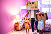 Portrait of father and daughters playing with cardboard box on head in the bedroom at home