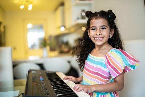 Portrait of a child girl playing digital piano keyboard at home