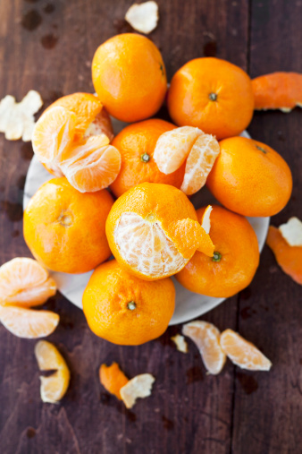 Fresh clementines, half-eaten, in a pile on a wood table.