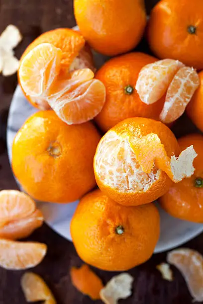Freshly-picked clementines, both whole and partially-eaten, scattered on a wood table.