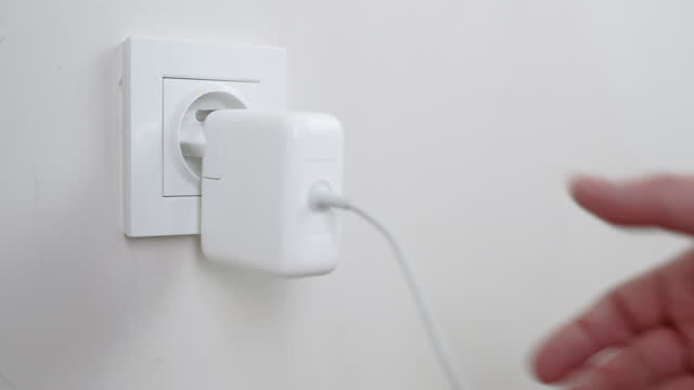 Male hand plugging and unplugging plug into white wall socket. Close-up power socket, charger cable