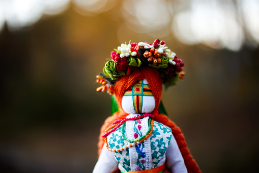 Rag doll on the background of the autumn forest. National traditional Ukrainian doll in a wreath in autumn.