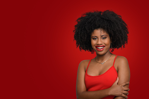 woman looks at camera and smiles, young woman with afro hairstyle and red clothes on red background