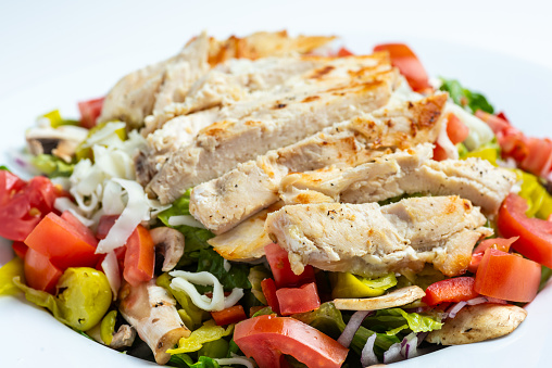 Close up Sliced grilled chicken breast over a greek salad