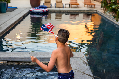 High quality stock photo of a multi-racial boy with an American Flag and Sparklers in an outdoor pool.