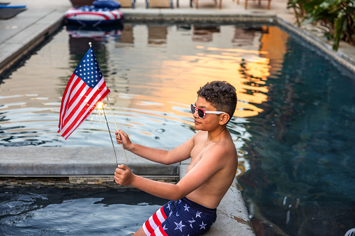 High quality stock photo of a multi-racial boy with an American Flag and Sparklers in an outdoor pool.