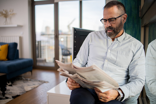 Mature man sitting and reading newspaper at home