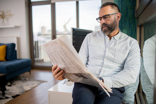 Mature man sitting and reading newspaper at home