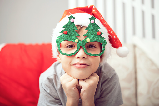 Portrait of happy, laughing, smiling Caucasian child boy in Santa hat and funny glasses with Christmas trees. The concept of Merry Christmas and New Year