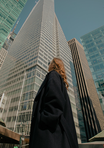 A woman with her back looking up at the skyscrapers from below.