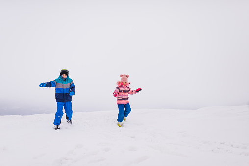 Winter portrait of a beautiful little boy and girl laughing and having a lot of fun in snow.