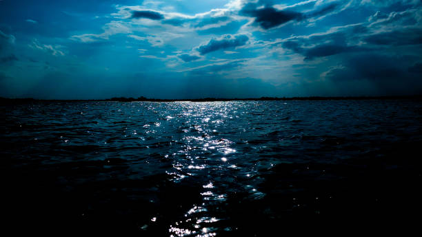 istock Deep blue moonlit ocean at night with calm waves make a great travel background vacation. Background bright rays of the moon through dramatic dark clouds over sea, light and reflection on the water 1656242647