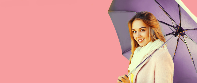 Portrait of beautiful happy smiling blonde woman with umbrella on pink background, blank copy space for advertising text