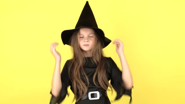 Little girl in witch costume on Halloween at yellow studio background