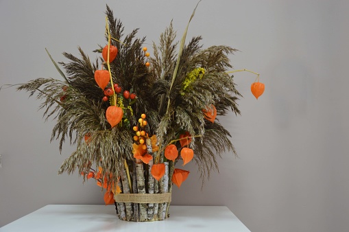 Beautiful decorative autumn bouquet with red and yellow flowers and dried flowers of grass and cereals on a table in the interior of the house.