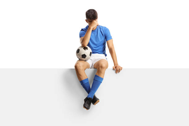 istock Disappointed football player sitting on a blank panel 1656423947