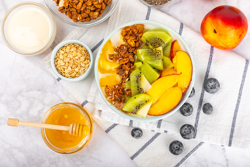 Granola bowl with yogurt and fresh almonds, blueberries, raspberries,peach and strawberries on a  kitchen table.Acai and spirulina bowl.Healthy breakfast concept.copy space.Place for text.