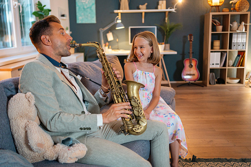 Single Caucasian father playing saxophone while his daughter listening to him