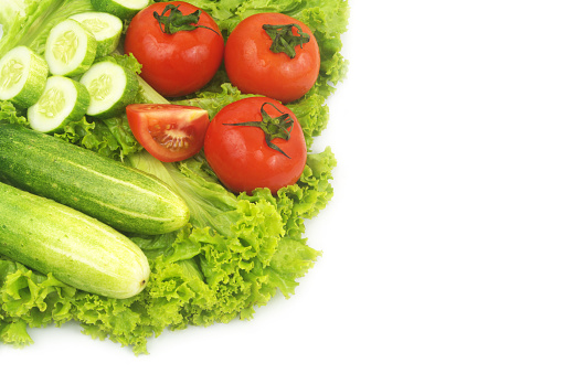 Fresh cucumbers and tomatoes on salad leaves background isolated on white. Copy space for text.