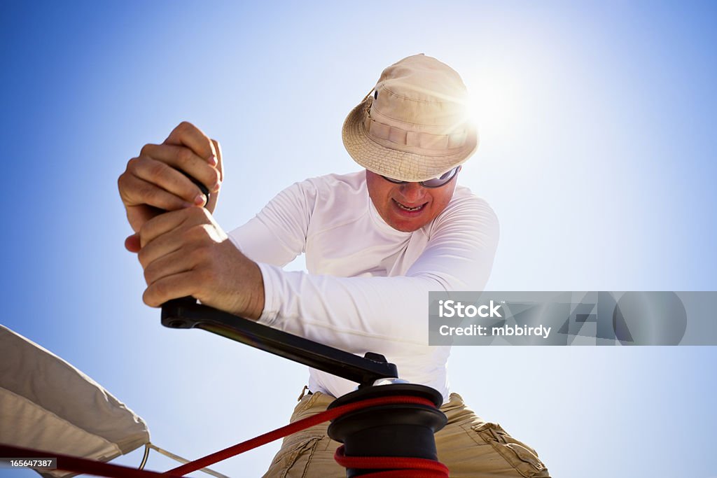 Sailor winding rope with winch Sailor winding rope of foresail with rotating crank on winch. Sailing Team Stock Photo