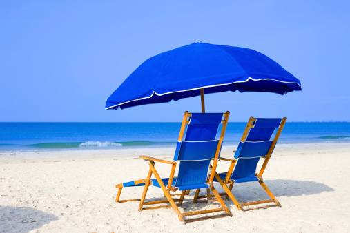 White sandy beach with two blue beach loungers and umbrella