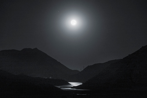 Super Full Moon reflecting its moonlight over the river in between the dark Mountains with two small towers at the end. Jajrood River close to Latyan Dam one of the main sources of water for Tehran, On 30th of August, 2023