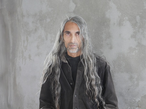 Man with long silver hair and goatee pudding in front of gray wall